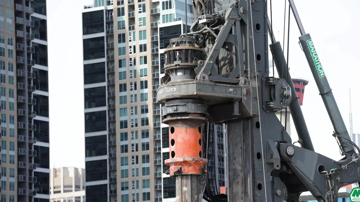 Orange-collared drill rig against downtown Calgary towers